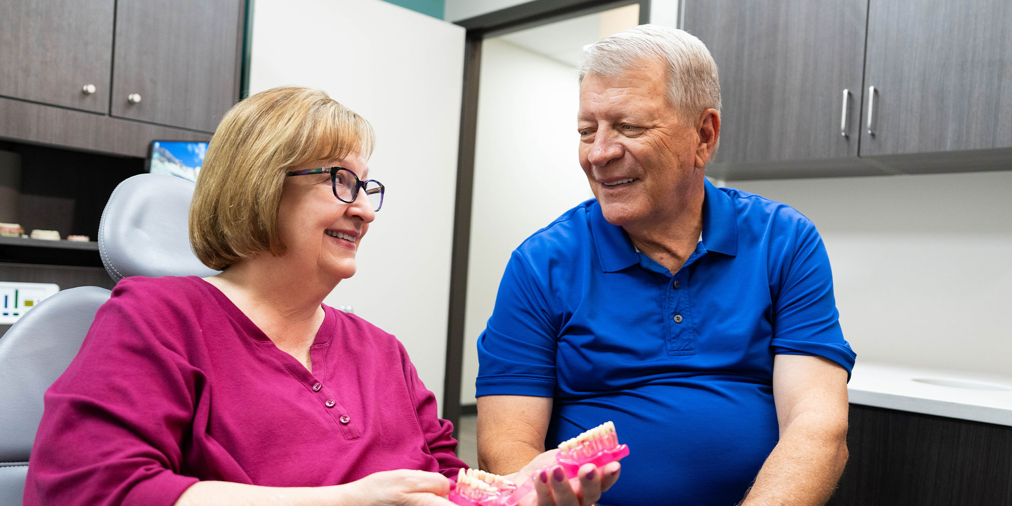 patient and their partner smiling while holding a full arch dental model within the dental center