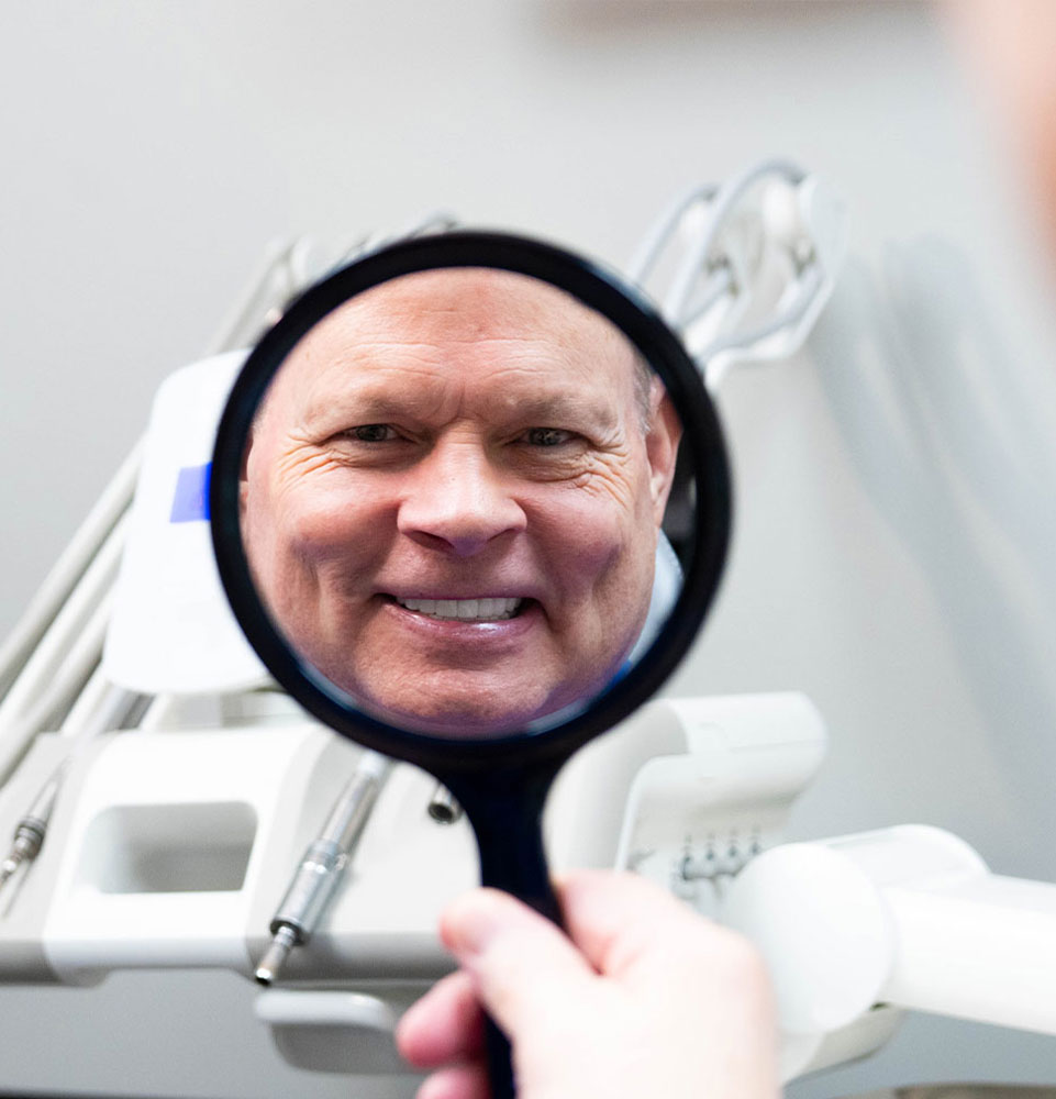 patient smiling brightly within handheld mirror