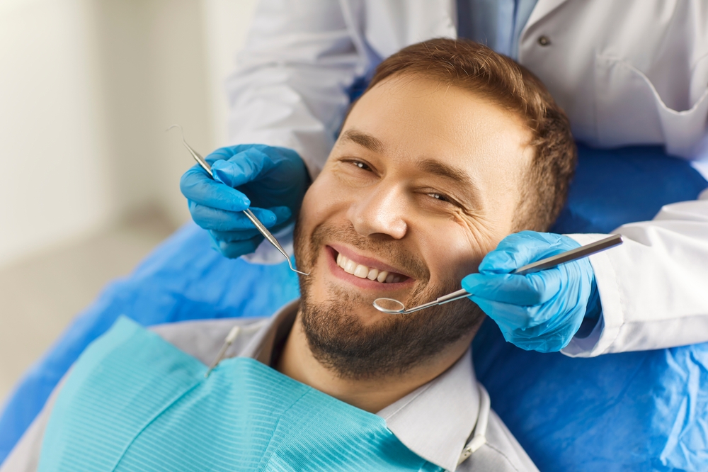 man in dental chair with dental tools by his mouth doctor behind him